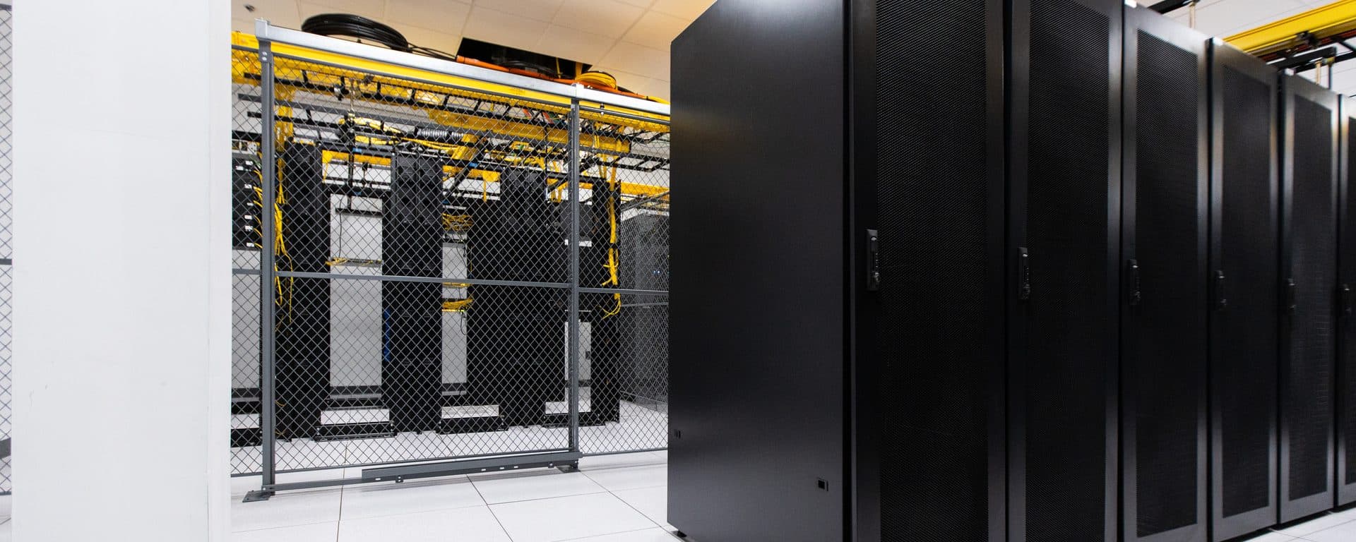 Customer colocation cage with server racks behind a steel mesh in a tym2 data hall